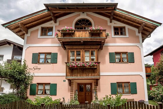 Vorderansicht des Haus Savoy mit rosa Fassade, Holzbalkonen und grünen Fensterläden.