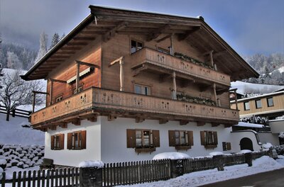 Haus Obernauer im Winter Zweistöckiges Alpenhaus mit Holzfassade, Balkonen und weißem Erdgeschoss in verschneiter Landschaft.