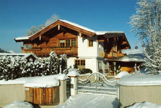 Villa Kitz Winteransicht Alpines Wohnhaus mit Holzfassade und schneebedecktem Dach hinter einem weißen Metalltor im Winter.