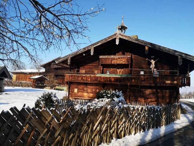 Historisches Bauernhaus im Winter Traditionelles Bauernhaus aus dunklem Holz mit Holzzaun im Schnee unter blauem Himmel.