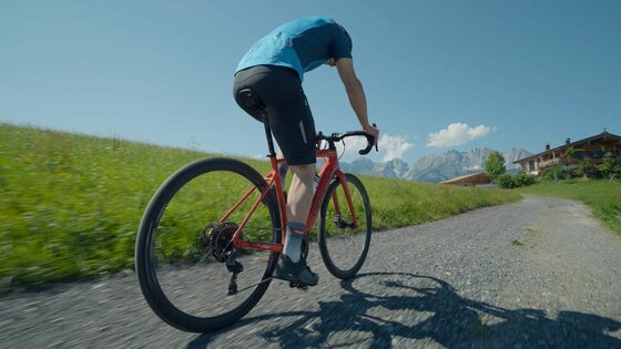 Ein Radfahrer auf einem roten Gravelbike fährt einen Schotterweg entlang.