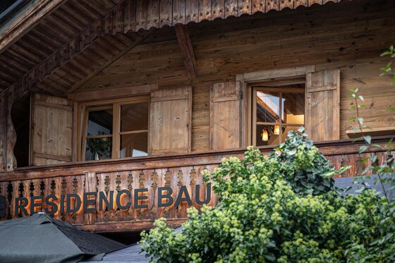 Hausansicht Resi's Kitz Lodge Holzfassade eines alpinen Gebäudes mit Balkon, Fenstern und dem Schriftzug Residence Bau.