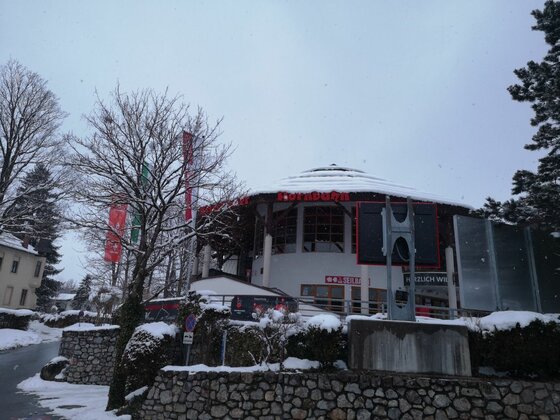 Bergbahnstation im Winter Rundes Gebäude der Bergbahn im Winter mit schneebedecktem Dach und umliegenden Bäumen.