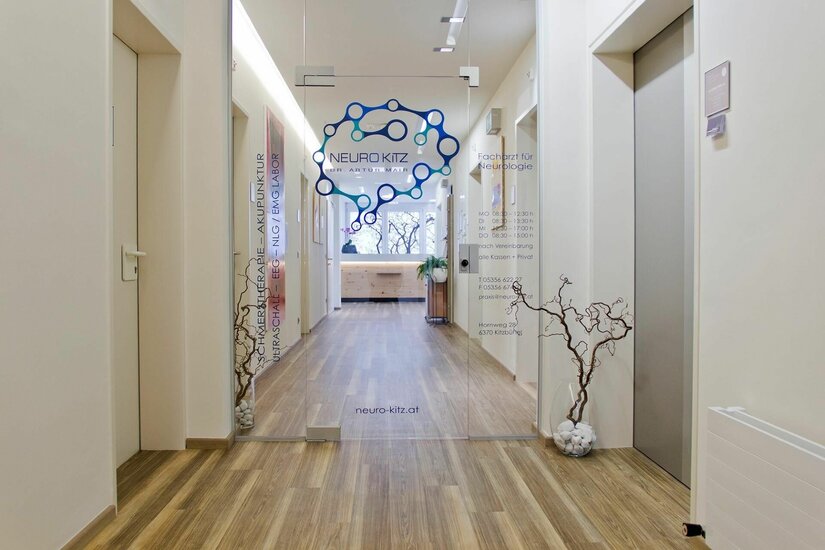 Eingang Neurokitz Dr. Mair Eingangsbereich einer Arztpraxis mit Glastür, Logo Neuro Kitz und hellem Holzboden.
