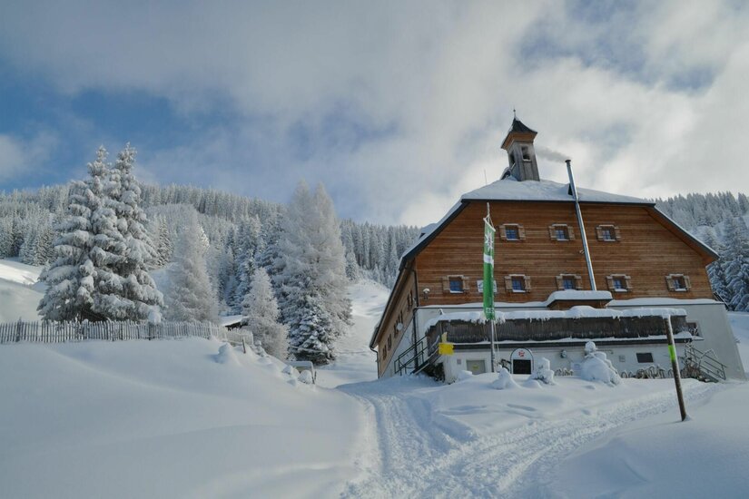Berghütte Kelchalm im Winter Holzhütte mit Glockenturm in verschneiter Winterlandschaft vor bewaldetem Hang.