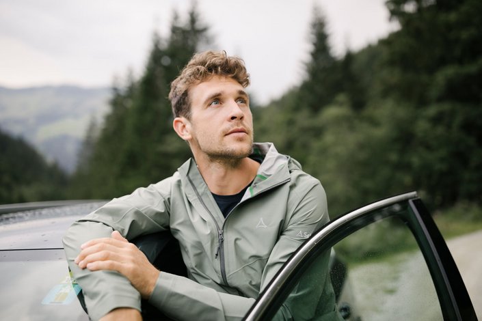 Mann steht vor seinem Auto im Wald und lehnt scih an