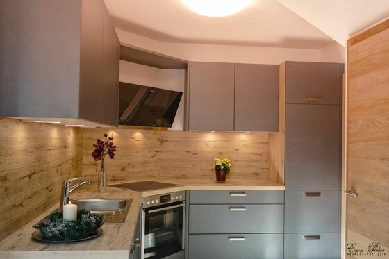 Küche im Hoamatl Jochberg Moderne Einbauküche in Grau und Holzoptik mit Herd, Spüle und beleuchteter Arbeitsplatte.
