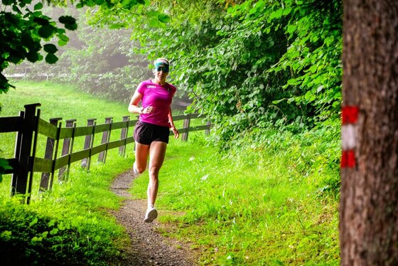 Lisa Hauser beim Lauftraining Eine Frau in Sportkleidung läuft auf einem schmalen Waldpfad neben einem Holzzaun.