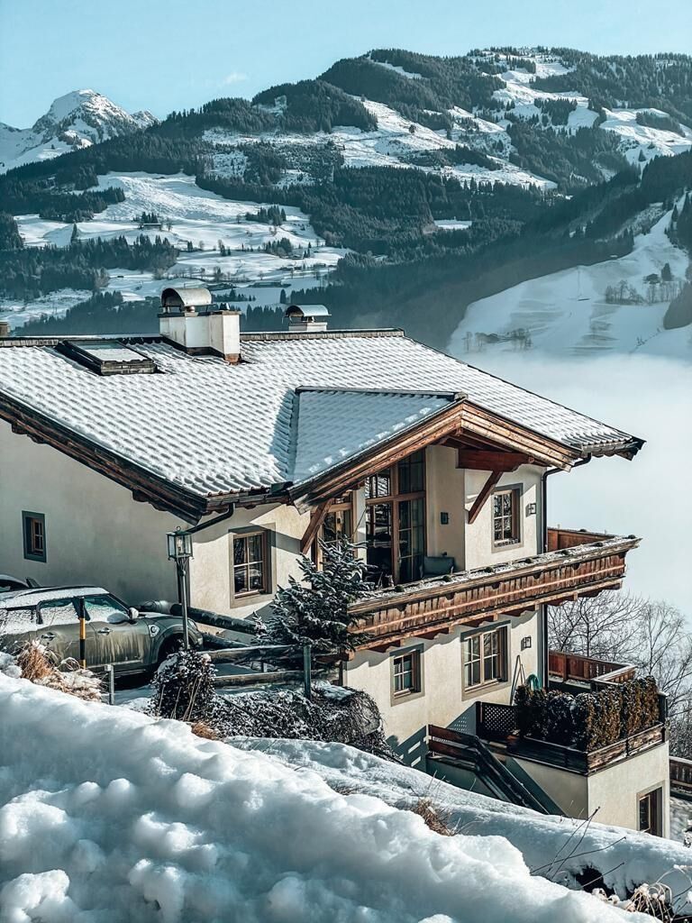 Residenz am Berg - Winter Alpines Wohnhaus mit Holzbalkon und schneebedecktem Dach vor verschneiter Bergkulisse.