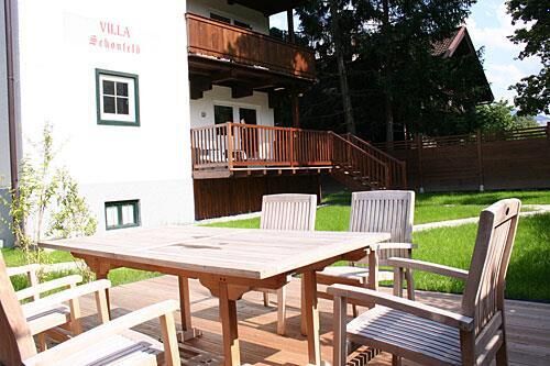 Garten der Villa Schönfeld Holztisch und Stühle auf einer Terrasse vor der Villa Schönfeld mit angrenzender Rasenfläche.