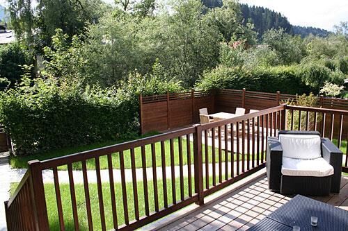 Balkon der Villa Schönfeld Holzterrasse mit Gartenmöbeln, Geländer und Blick auf eine Rasenfläche mit Hecke.