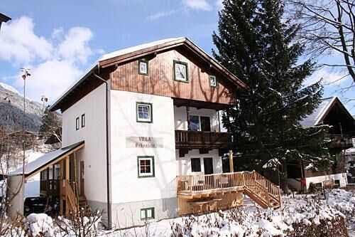 Villa Schönfeld im Winter Zweistöckiges weißes Gebäude mit Holzgiebel und Balkon in einer verschneiten Winterlandschaft.