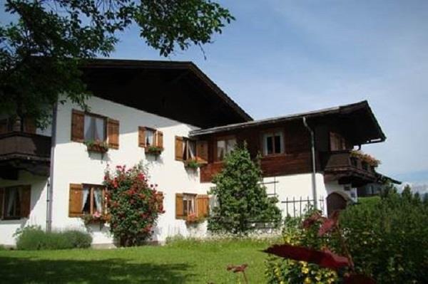 Haus hinten App. Hölzl Zweistöckiges alpines Wohnhaus mit weißen Wänden, Holzfensterläden und Balkonen vor einer Wiese.