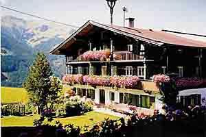 Alpines Haus im Sommer Mehrstöckiges Holzhaus mit blumengeschmückten Balkonen vor einer Bergkulisse.