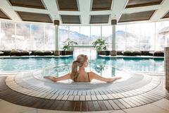 <p>Der Spa Bereich vom Grand Tirolia Kitzbühel mit einem großen Pool und Blick auf die Kitzbüheler Berge. Eine Frau sitzt am Rand des Pools und genießt die ruhige Atmosphäre.</p>