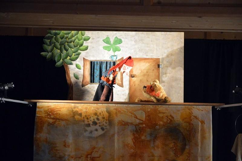 Kasperltheater für Kinder Eine Kasperl-Puppe und ein Stoffbär auf einer kleinen Theaterbühne mit gemaltem Hintergrund.