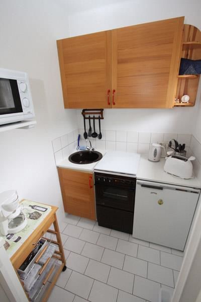 Kompakte Küchenzeile Kleine Küchenzeile mit Holzschränken, Herd, Spüle, Kühlschrank und Mikrowelle auf weißem Fliesenboden.