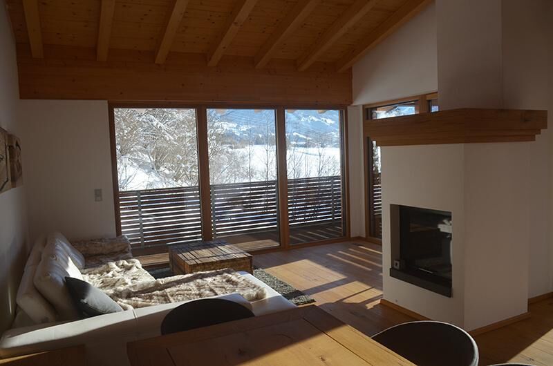 Wohnraum Apartment Hofer Manfred Moderner Wohnraum mit Sofa, Kamin und großem Panoramafenster mit Blick auf eine verschneite Winterlandschaft.