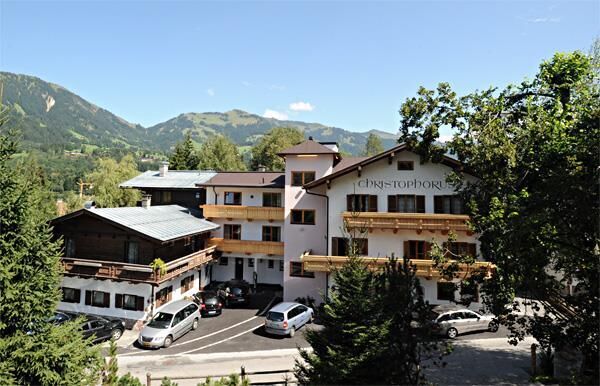 Haus Sommer Christophorus Mehrstöckiges Hotelgebäude mit Holzbalkonen und Parkplatz vor bewaldeter Bergkulisse.