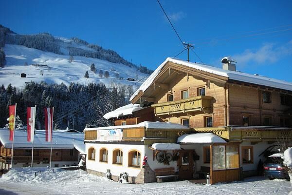 Jugendhotel Noichl in Aurach Ein mehrstöckiges Holzhaus mit schneebedecktem Dach vor einem bewaldeten Berghang im Winter.
