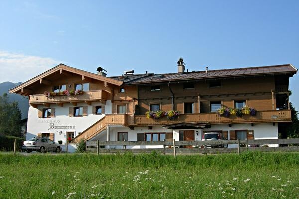 Landhaus Sommerau im Sommer Zweistöckiges Landhaus mit Holzbalkonen und Blumenschmuck vor einer Wiese.
