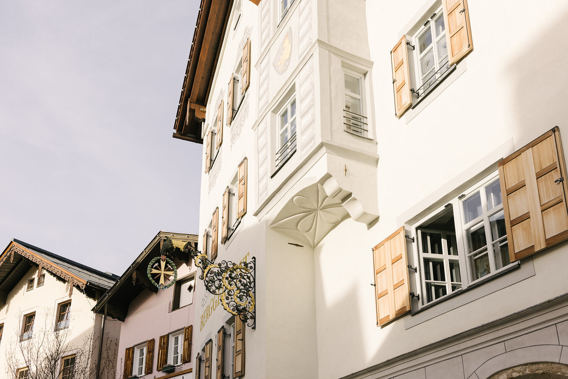 Ein charmantes Stadtbild mit traditionellen Holzbalkonen und einem kunstvollen Wirtshausschild in Kitzbühel.